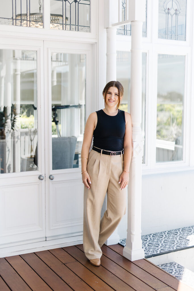 Ashleigh Power, Newcastle Australia Professional Graphic Designer standing outside white old home leaning on door