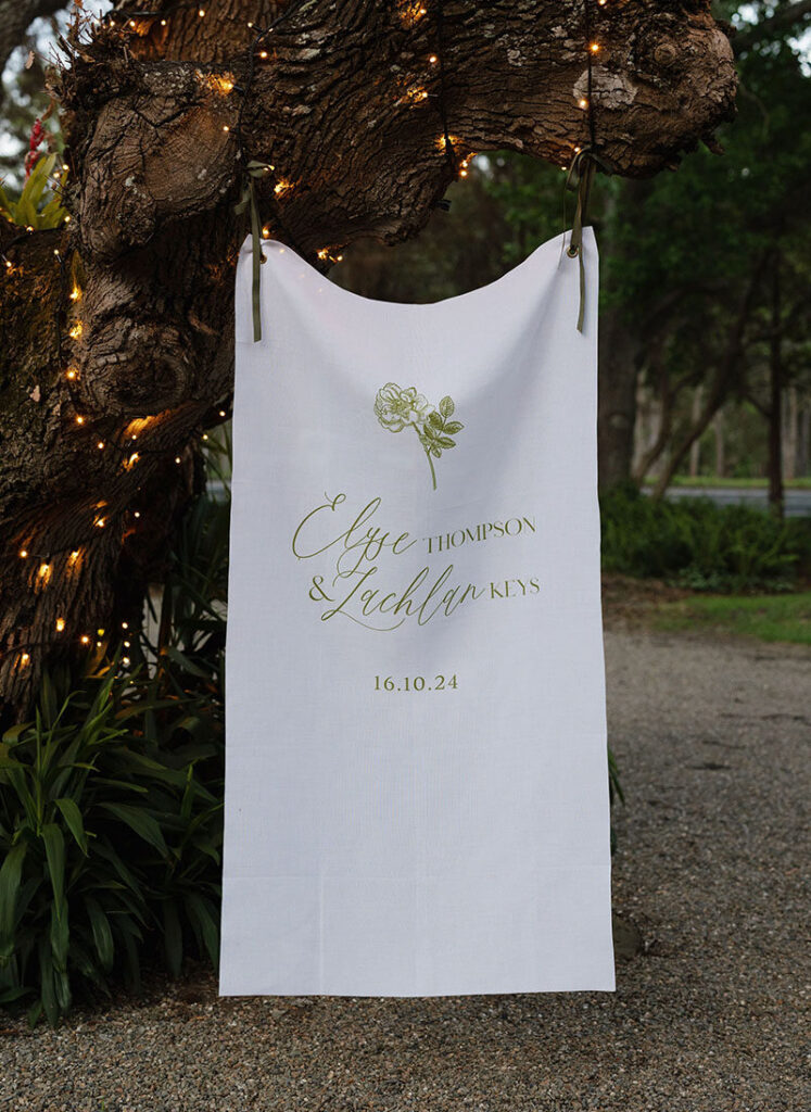 Linen wedding welcome sign hanging from tree and blowing in the breeze. Custom wedding signage.