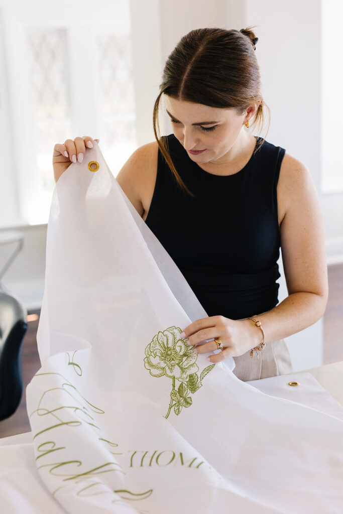 Woman looking down and holding linen wedding welcome sign with green text and floral outline