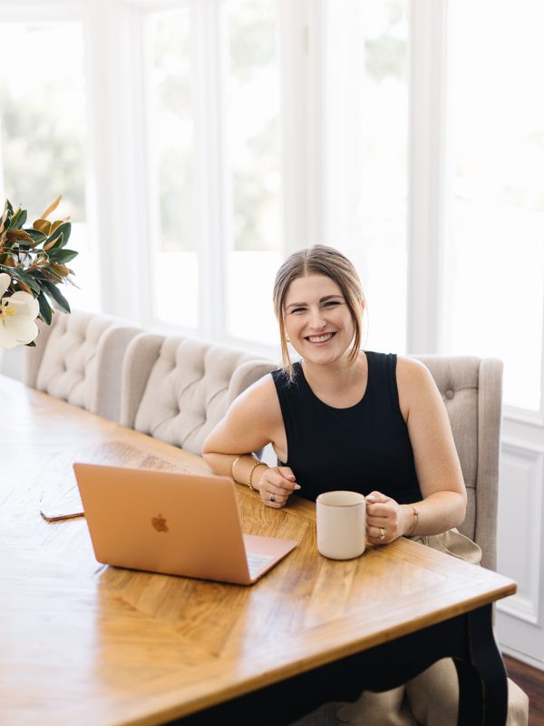 Ashleigh at desk with laptop and a cup of tea looking at the camera with a friendly smile